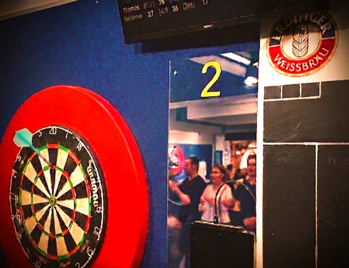 Dartboard im Clubraum des Dartclub Gamsen 1996, im Hintergrund Mitglieder beim Spielabend