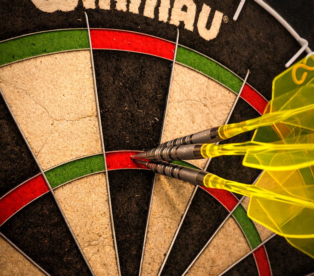 Nahaufnahme eines Dartboards: drei Darts stecken dicht beieinander im Feld der 20
